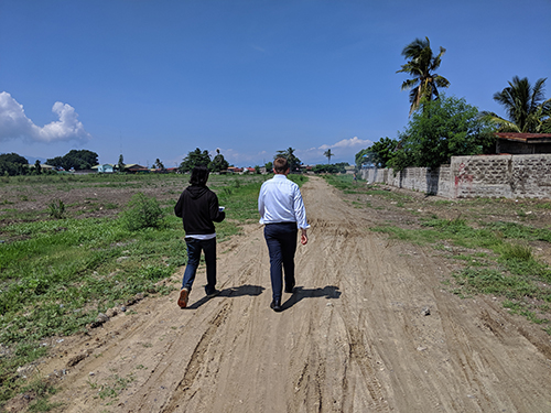 Two men walking at a muddy road next to a emplty grassfield